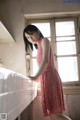 A woman in a red dress leaning against a window.