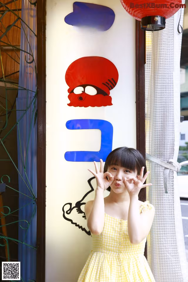 A little girl in a yellow dress standing in front of a sign.