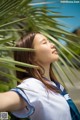 A woman in a white shirt and blue scarf leaning against a palm tree.