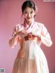 A woman in a pink and white hanbok poses for a picture.