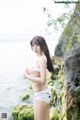 A woman in a white bikini standing on a rock by the water.