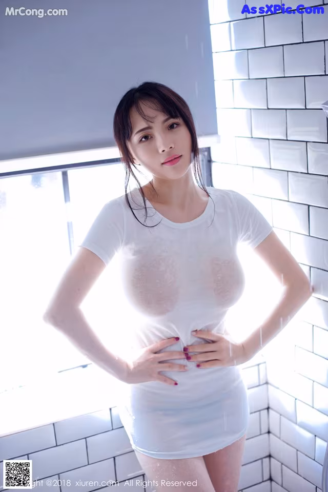 A woman in a white shirt standing in a bathroom.